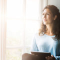 Thoughtful young woman holding digital tablet by window