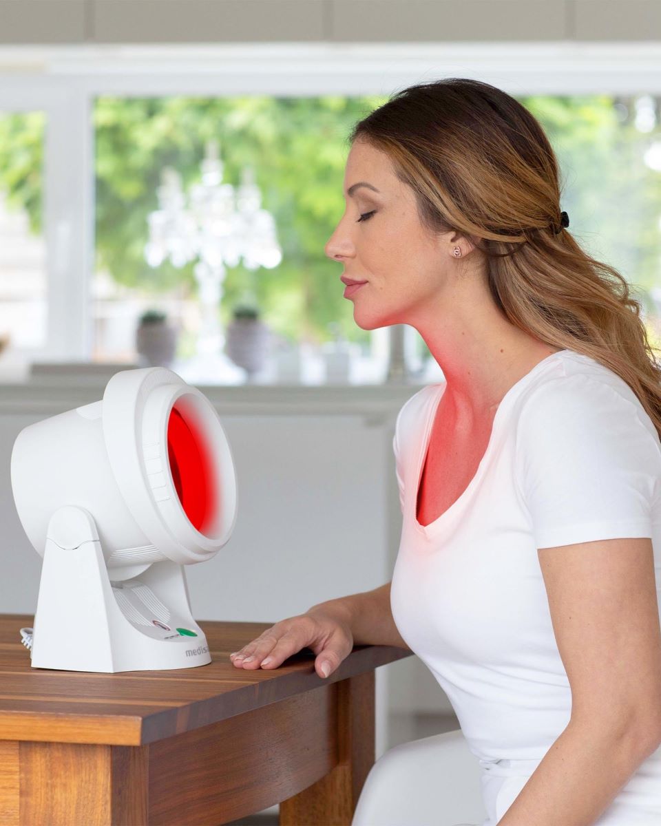 Person using the medisana infrared lamp for targeted heat application on the face