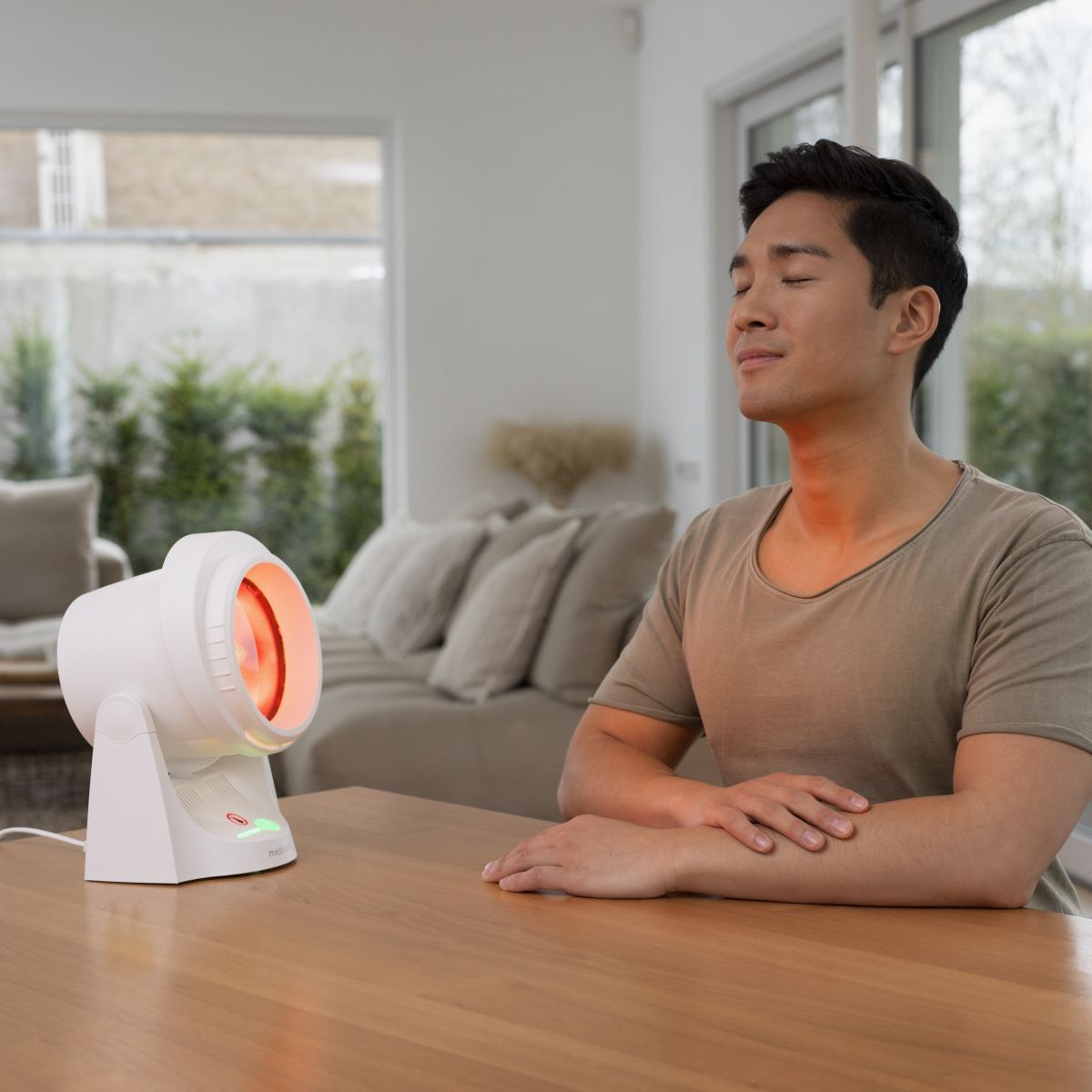 Person sitting comfortably in front of the medisana infrared lamp during a heat application