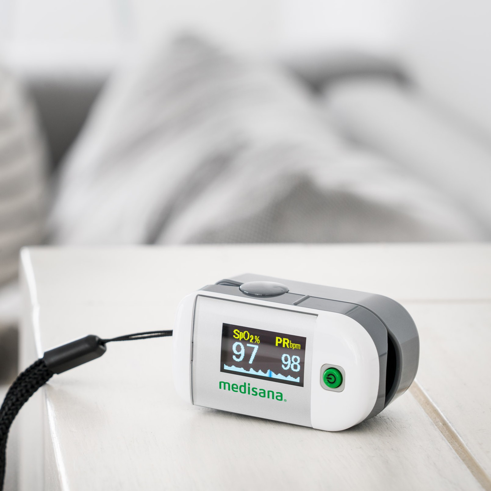 A white medisana pulse oximeter placed on a table displaying oxygen saturation and pulse values.
