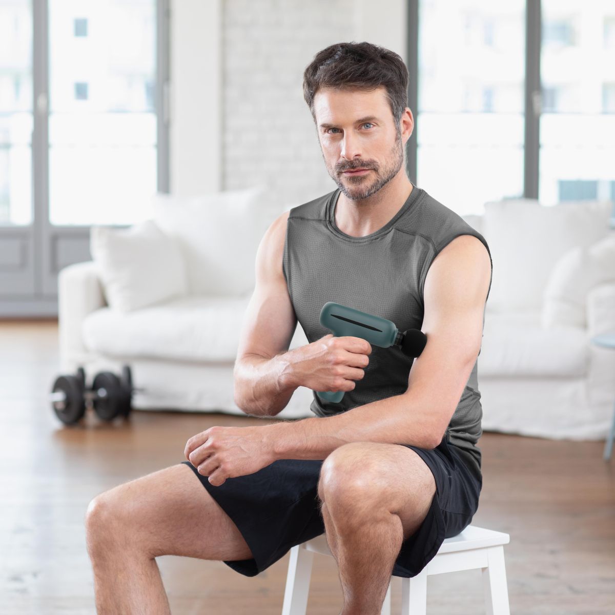 Man using medisana MG 200 massage gun on upper arm at home