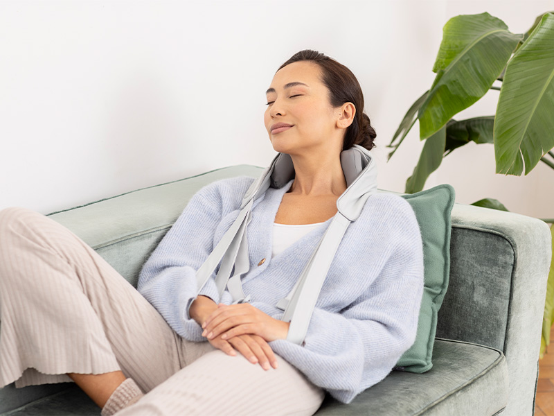 Woman relaxing with medisana NM 990 neck massager on the couch – cordless Shiatsu massage with heat function