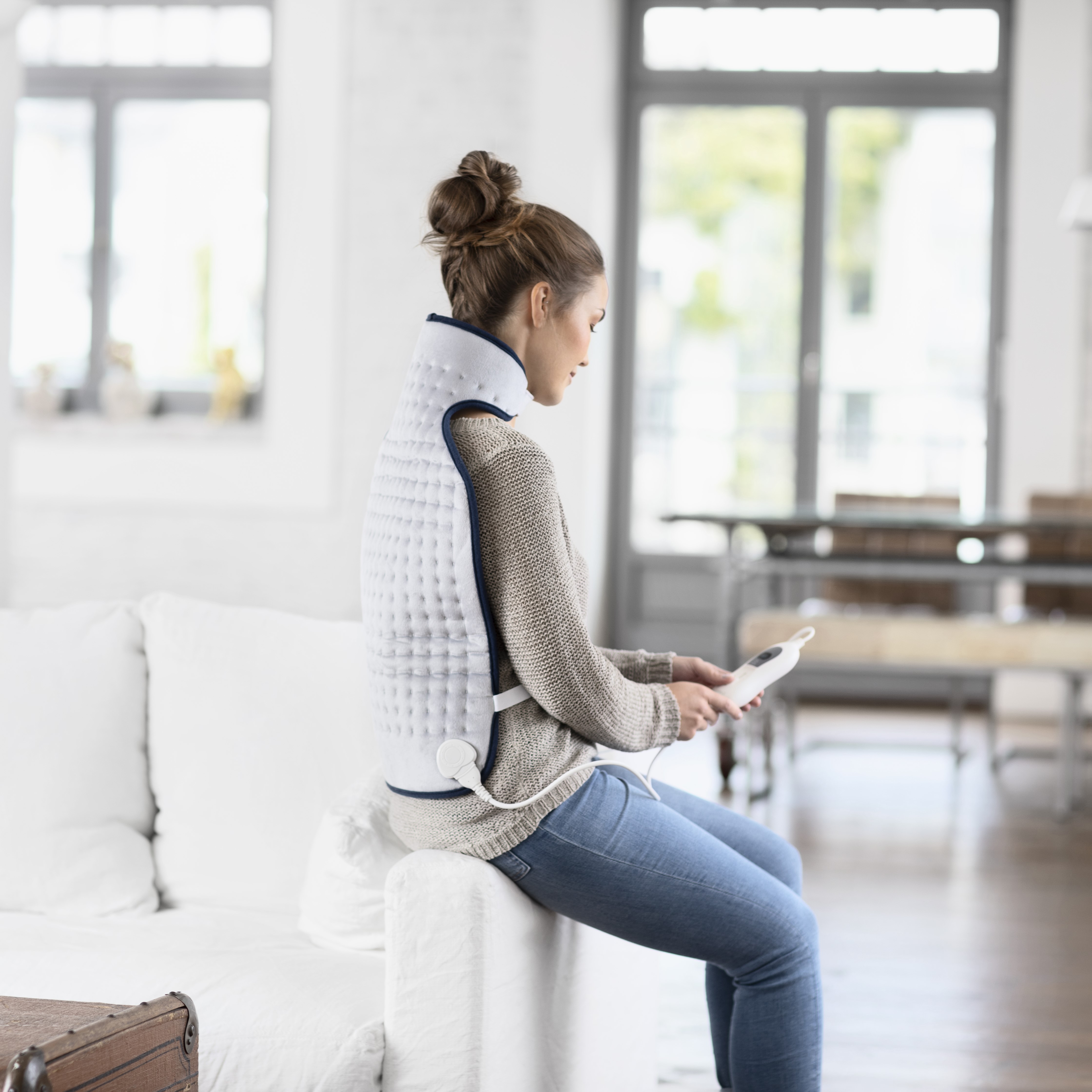 The user is wearing the neck warmer while sitting and enjoying soothing warmth that relaxes the neck and shoulder area.